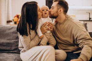 young family with baby toddler girl at home sitting on sofa